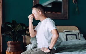 man with headache sits on bed