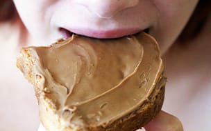 A young girl biting into a peanut butter sandwich