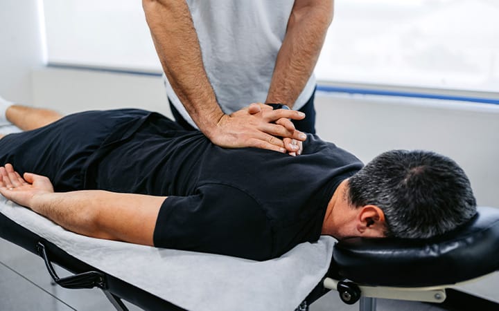 A chiropractor adjusting his male patient’s upper back